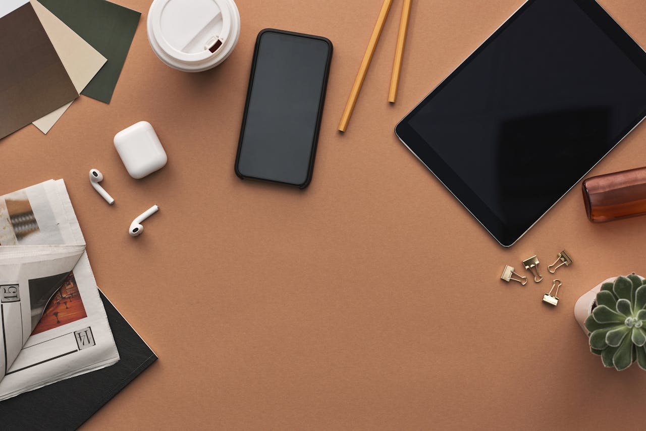 Top view of a stylish workspace with technology gadgets and stationery items on a brown background.