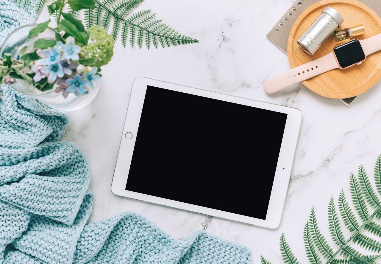 Flat lay of technology with tablet, watch, and plants on marble surface.