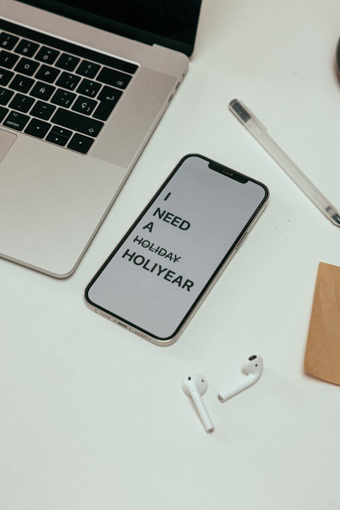 A clean minimalist workspace featuring a smartphone with text, laptop, and AirPods.
